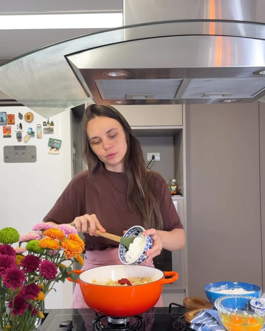 Tálita preparando uma torta de frango em panela laranja, com flores sobre a bancada